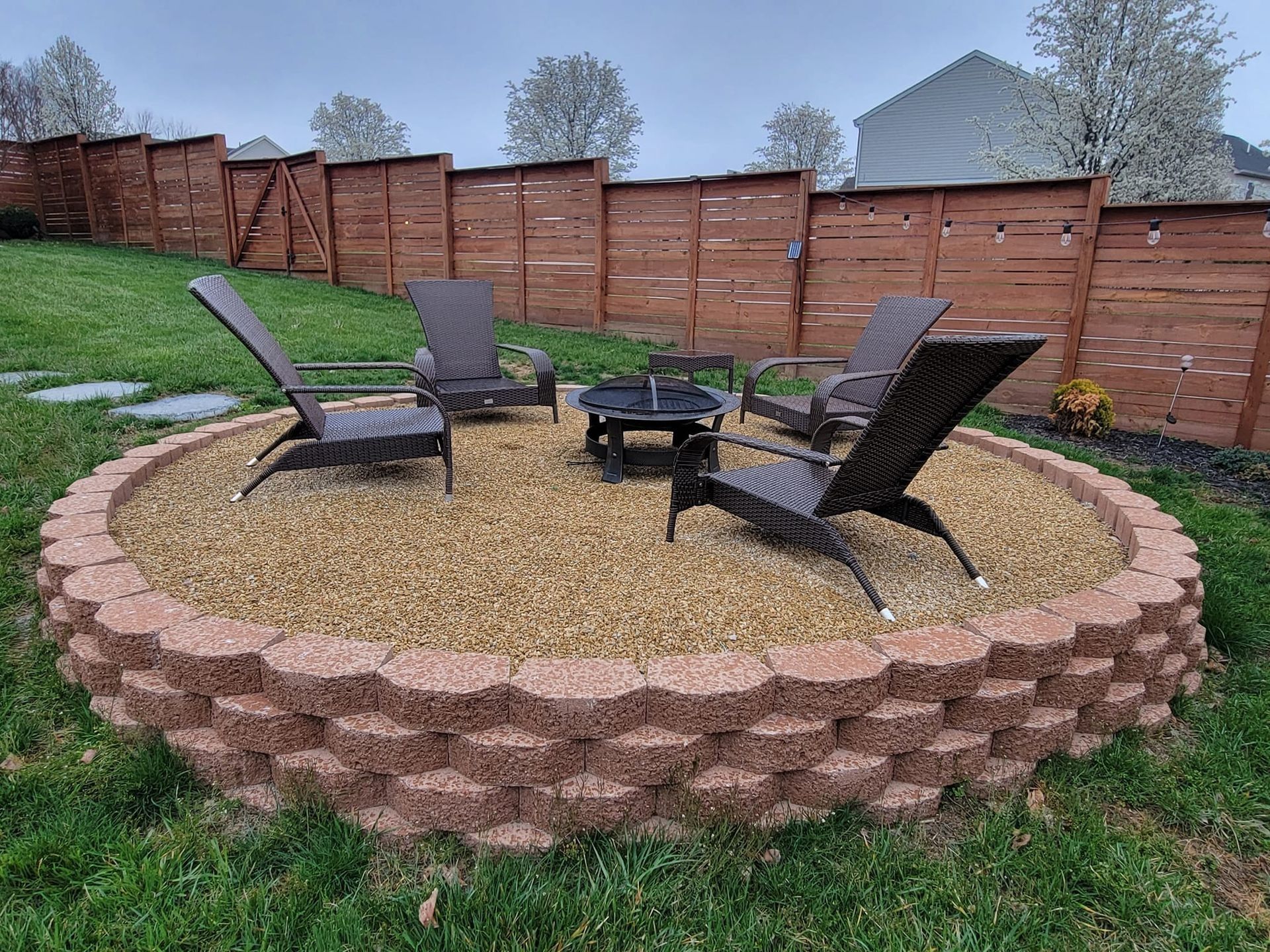 Backyard fire pit area with four chairs on a circular gravel patio and wooden privacy fence