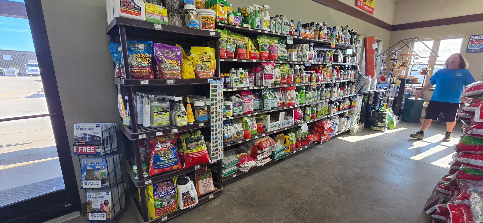 Convenience store aisle with snacks and candy shelves; shoppers near the back door in bright daylight