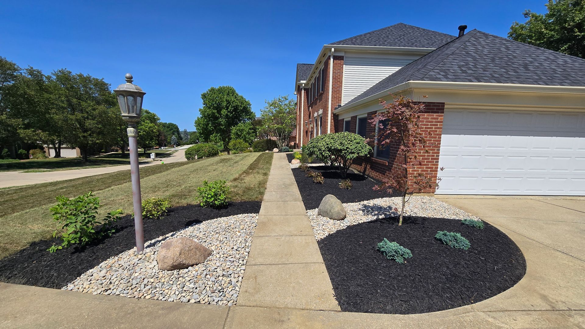 Suburban house entrance with brick facade, white garage, paved walkway, and landscaped front yard