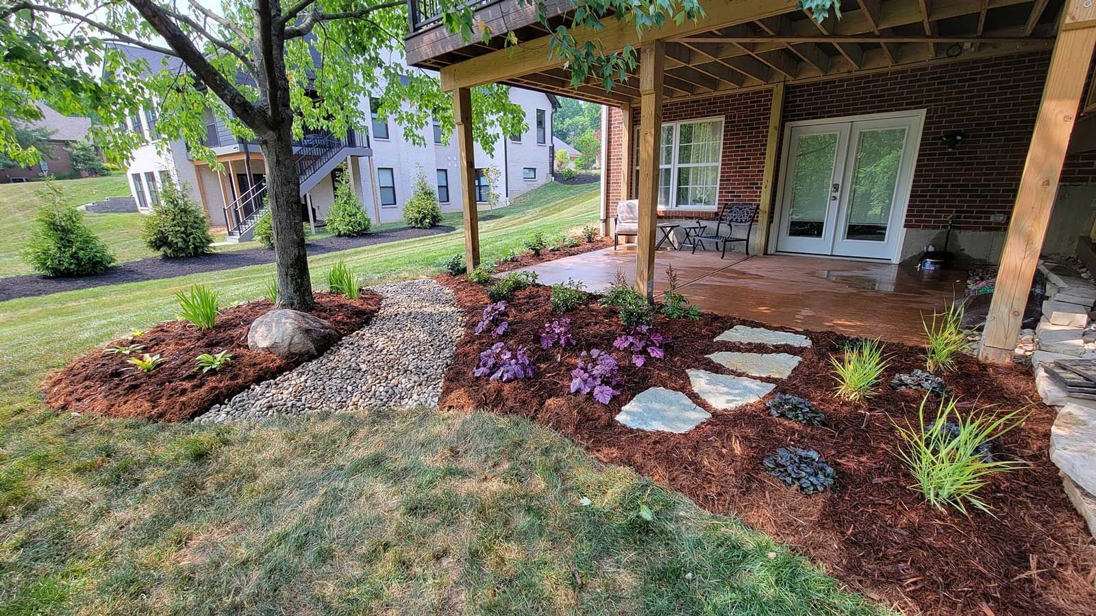 Landscaped front porch with mulch beds, stepping stones, and a hanging chair under a wooden patio cover.