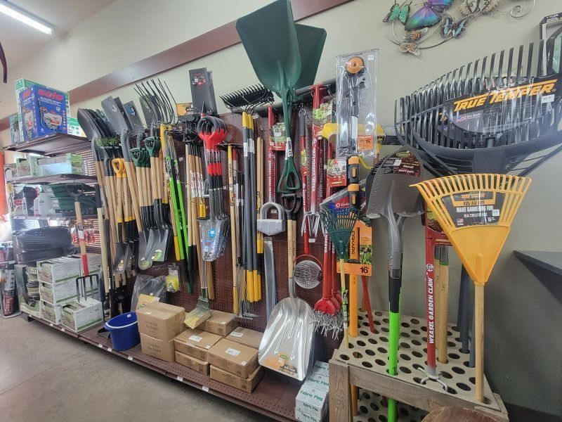 Garden tool aisle with rakes, shovels, and brooms displayed on shelves and hanging racks