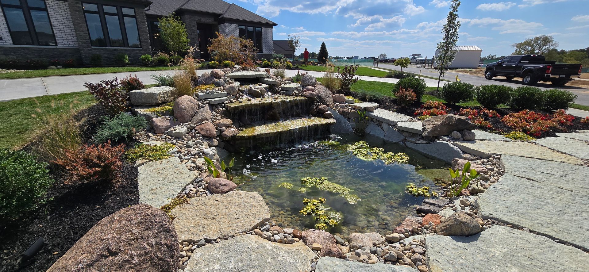 Tiered stone pond with lilies and cascading water in a landscaped garden under a blue sky