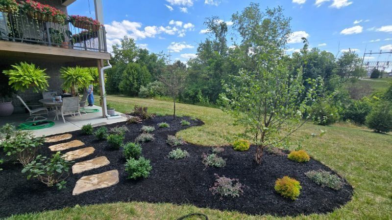 Landscaped backyard with stone steps, flower beds, and a small tree beside a house