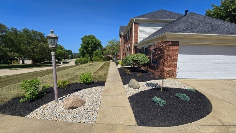 Landscaped suburban driveway with brick house, white garage, lamp post, and gravel planting beds