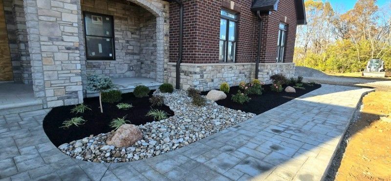 Stone house front entrance with curved paver walkway and landscaped mulch beds with white rock accents