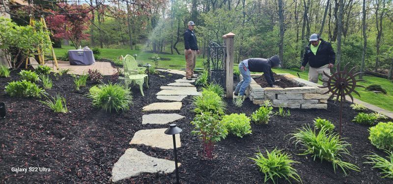 Garden path with stepping stones, raised beds, and two people working in the background