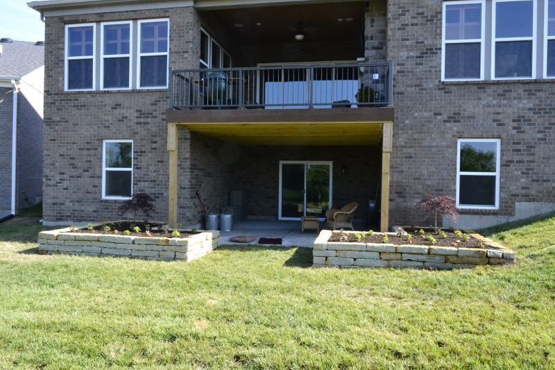 Stone house back patio with balcony and two raised garden beds on a grassy lawn.