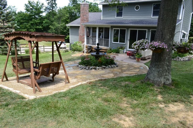 Backyard with wooden swing, patio, and gray house with flowering hanging baskets