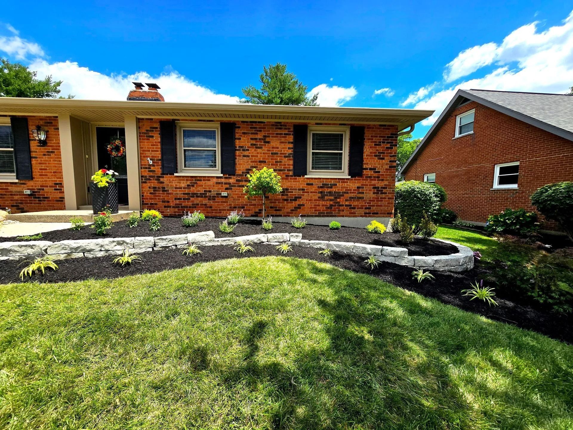 Brick ranch house with black shutters, landscaped front yard, and a bright blue sky
