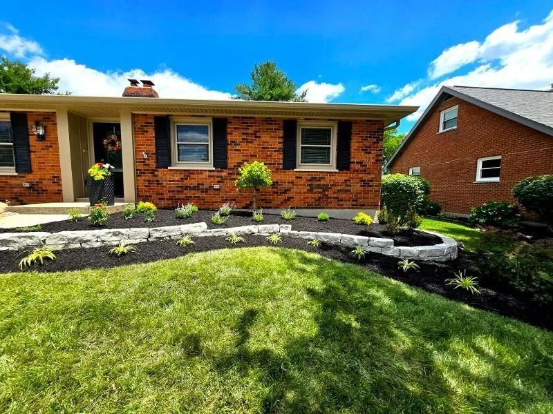 Single-story brick house with a curved stone garden border and green lawn under a bright blue sky