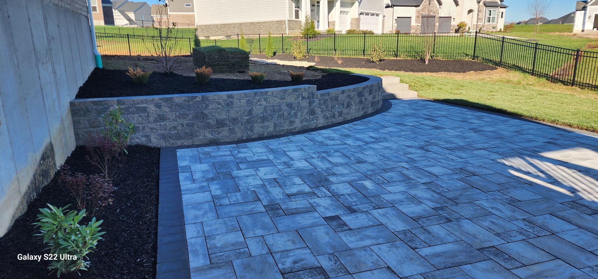 Stone patio and landscaped backyard with retaining wall, mulch beds, and neighboring houses in the background