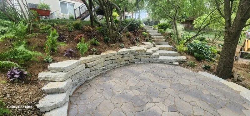 Curved stone patio with terraced steps and lush garden landscaping beside a house