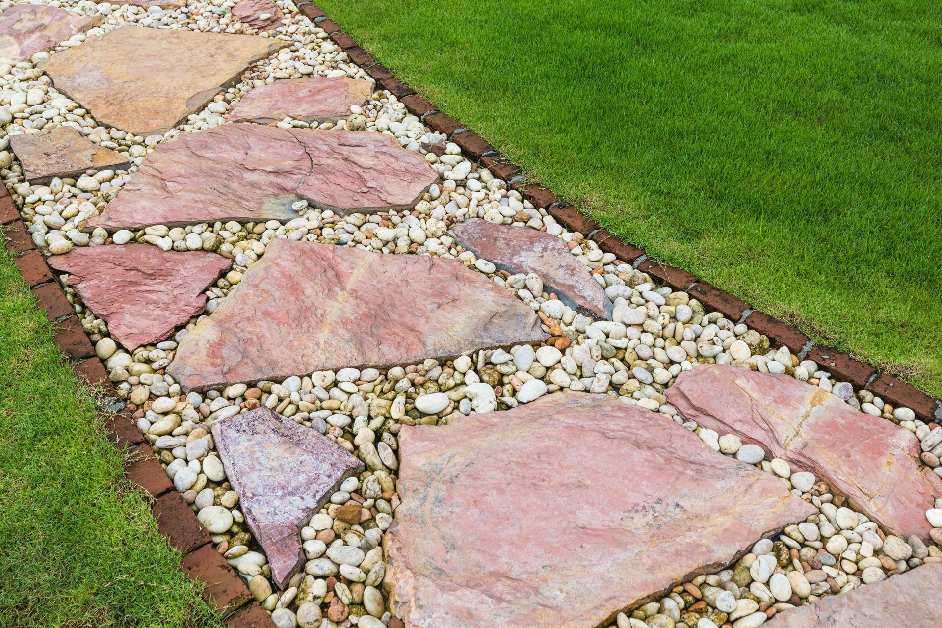 Pink stone mosaic garden path beside green grass