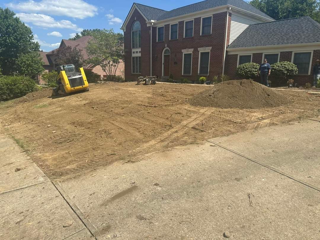 Fresh dirt and graded front yard beside a brick house, with a yellow skid steer on the left