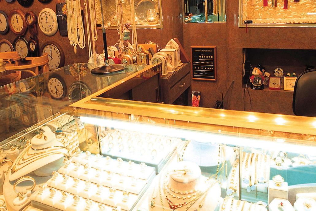 Warm, cluttered café counter with lit display case, shelves of teapots, and pastries in a cozy rustic interior