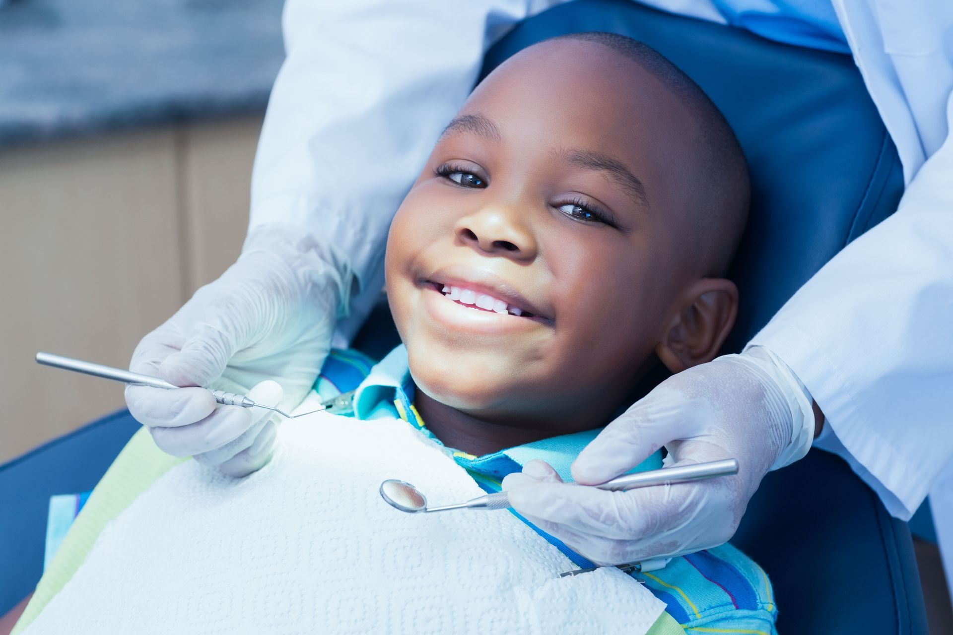 A person sitting in a dental chair smiling while a professional wearing gloves holds dental tools.