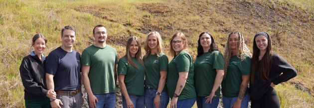 A person in safety glasses sits in a dental chair while a practitioner examines their teeth with a mirror and probe.