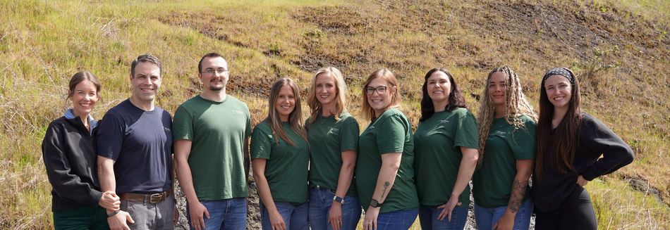 A person in safety glasses sits in a dental chair while a practitioner examines their teeth with a mirror and probe.