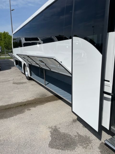 White tour bus with open storage compartments on a concrete surface