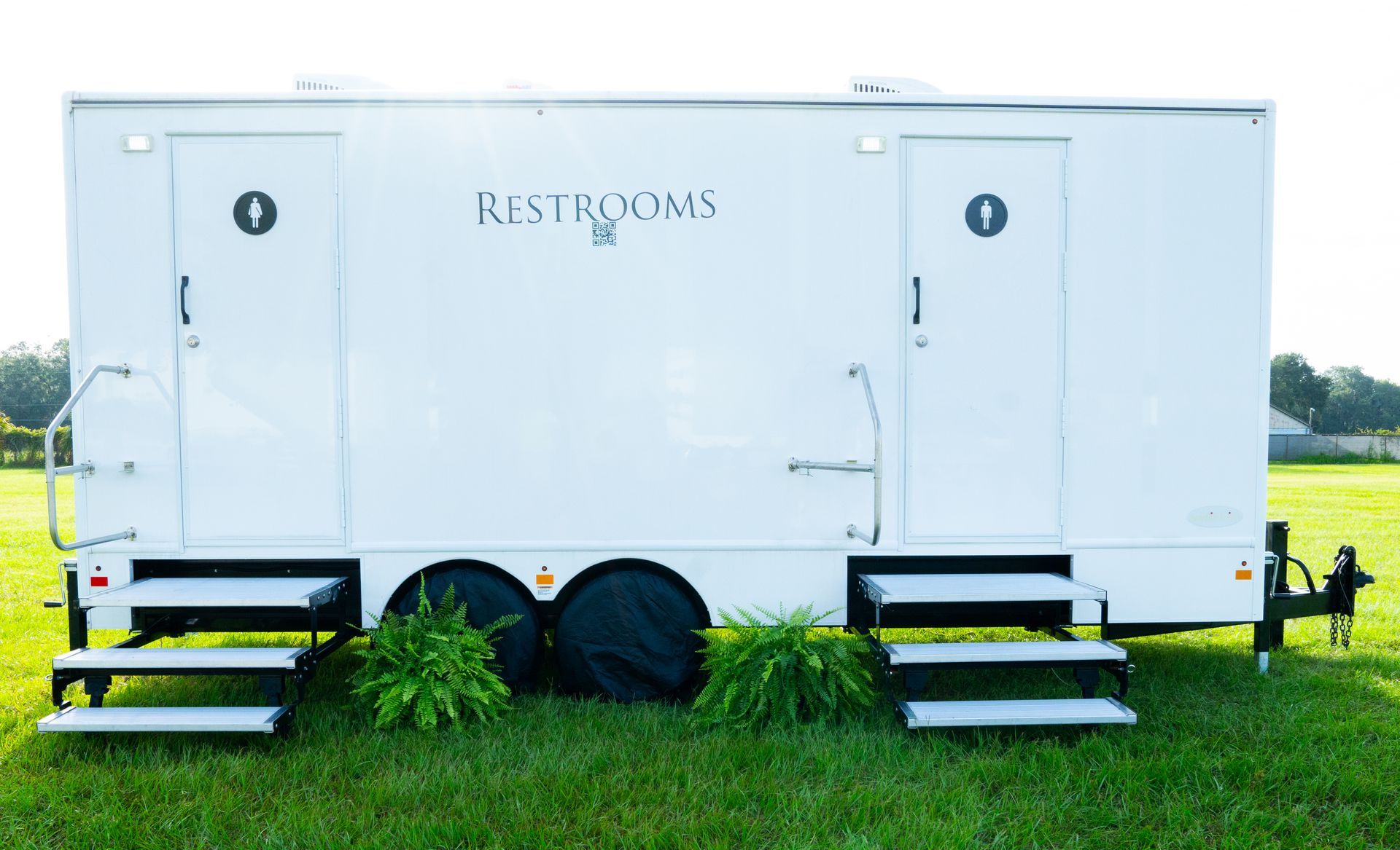A white restroom trailer is parked in a grassy field.