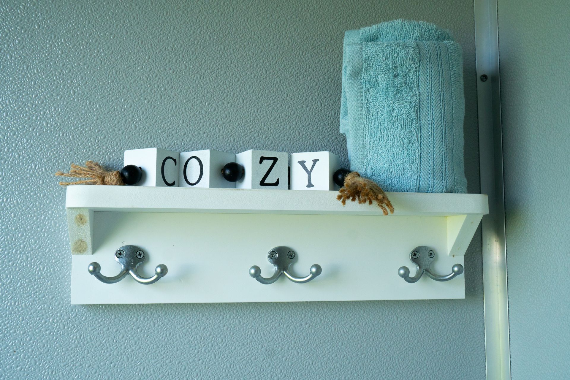 A white shelf with hooks and the word cozy on it