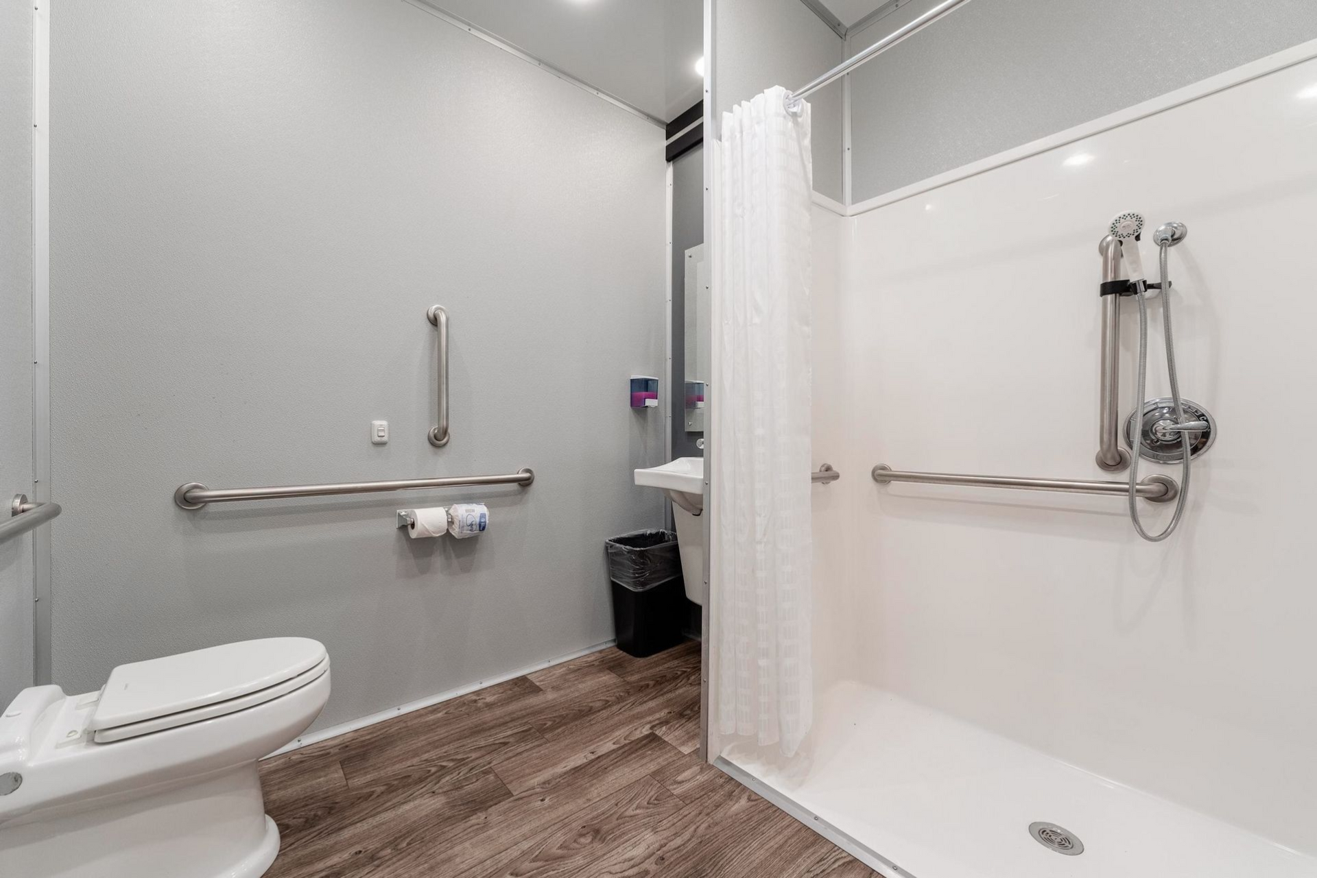 White shower stall and toilet in a small bathroom with a curtain. A small plant sits in the shower.