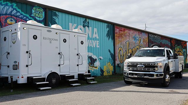 White service truck and equipment trailer parked beside a colorful graffiti wall outdoors.