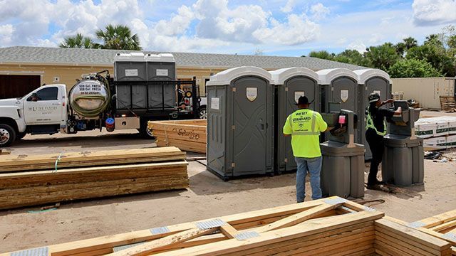 Construction site with workers near portable toilets and stacked lumber under a bright sky
