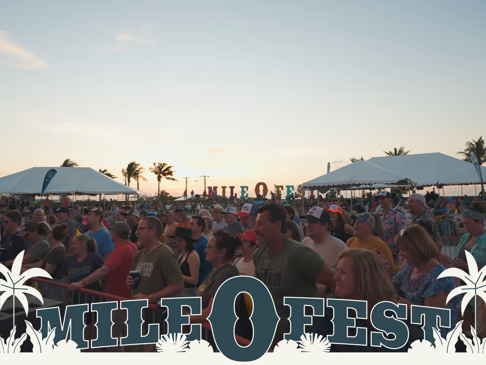 Crowd at Mile 0 Fest, outdoor music festival at sunset. People watching the stage under tents, palm trees in background.