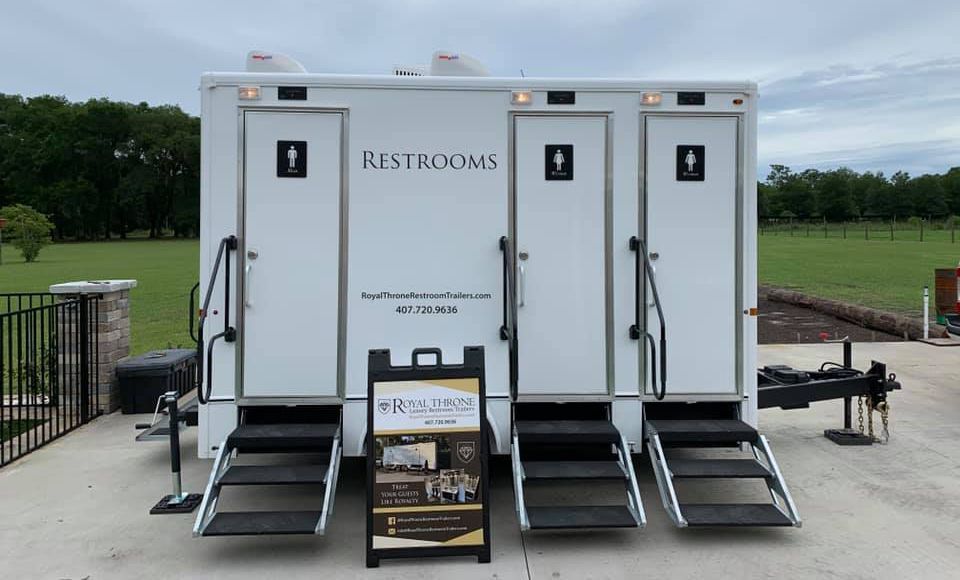 A trailer with three restrooms on it is parked in a parking lot