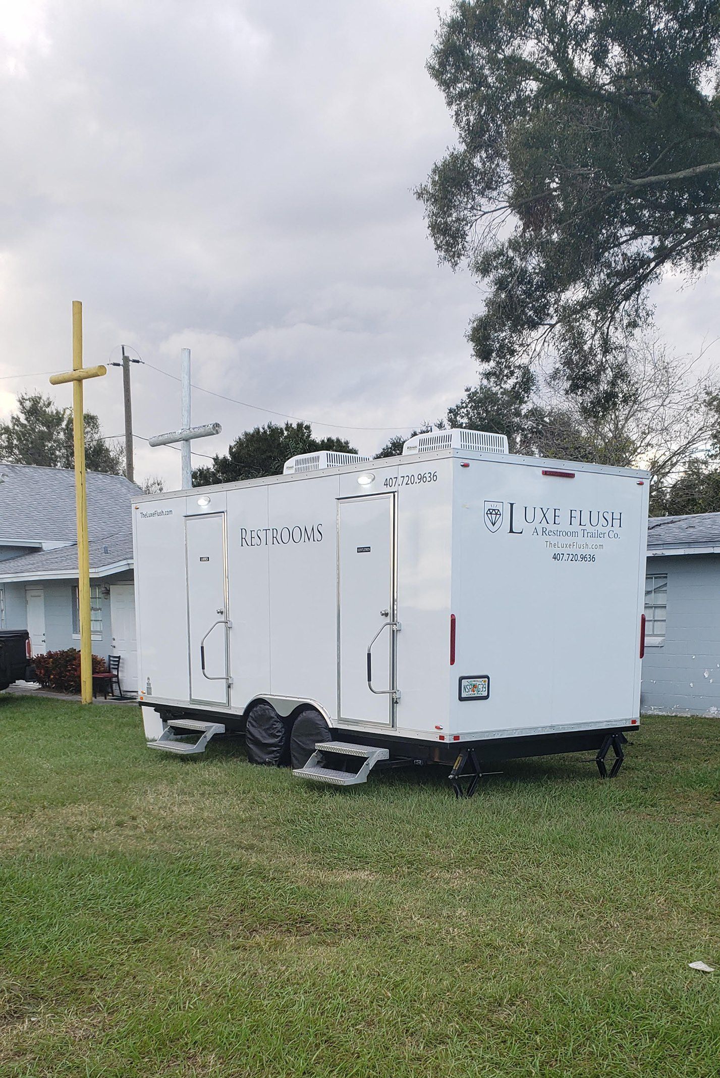 A white trailer is parked in a grassy field in front of a church