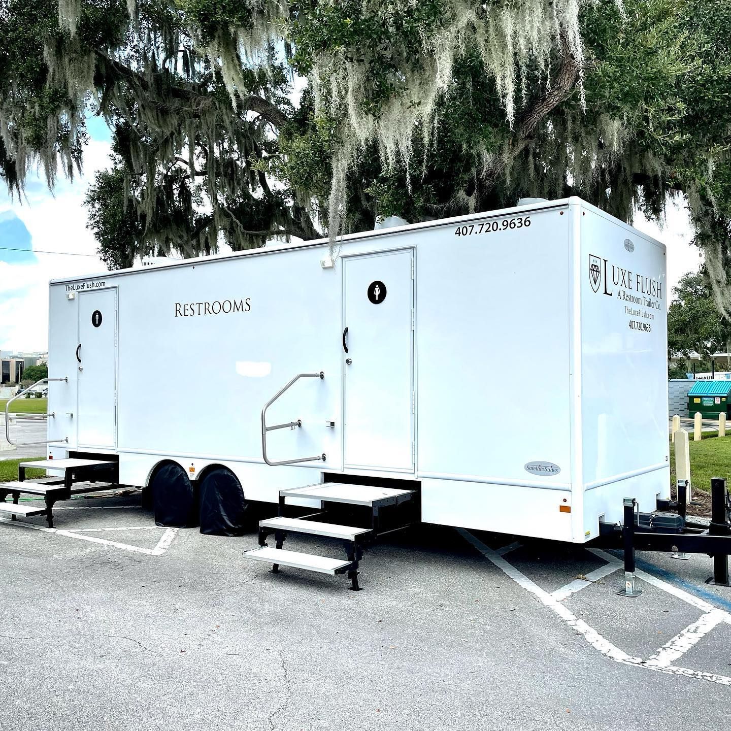 A white trailer is parked in a parking lot next to a tree