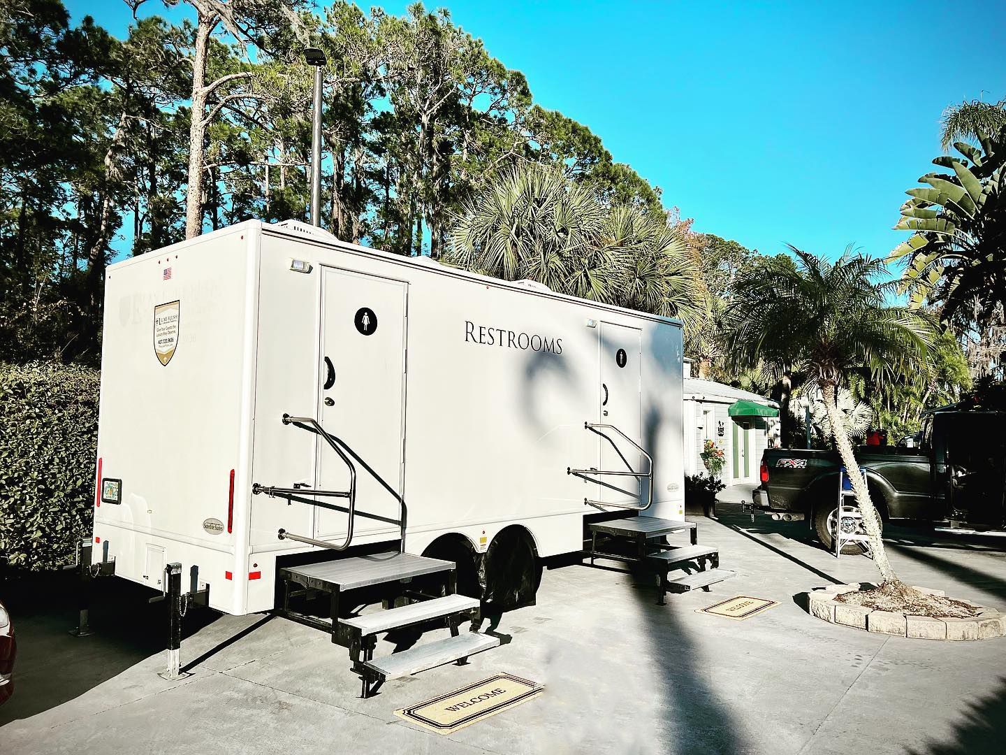 A white trailer is parked in a parking lot with trees in the background