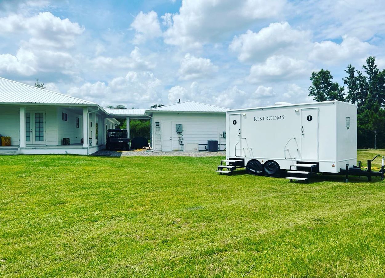 A white trailer is parked in a grassy field in front of a house
