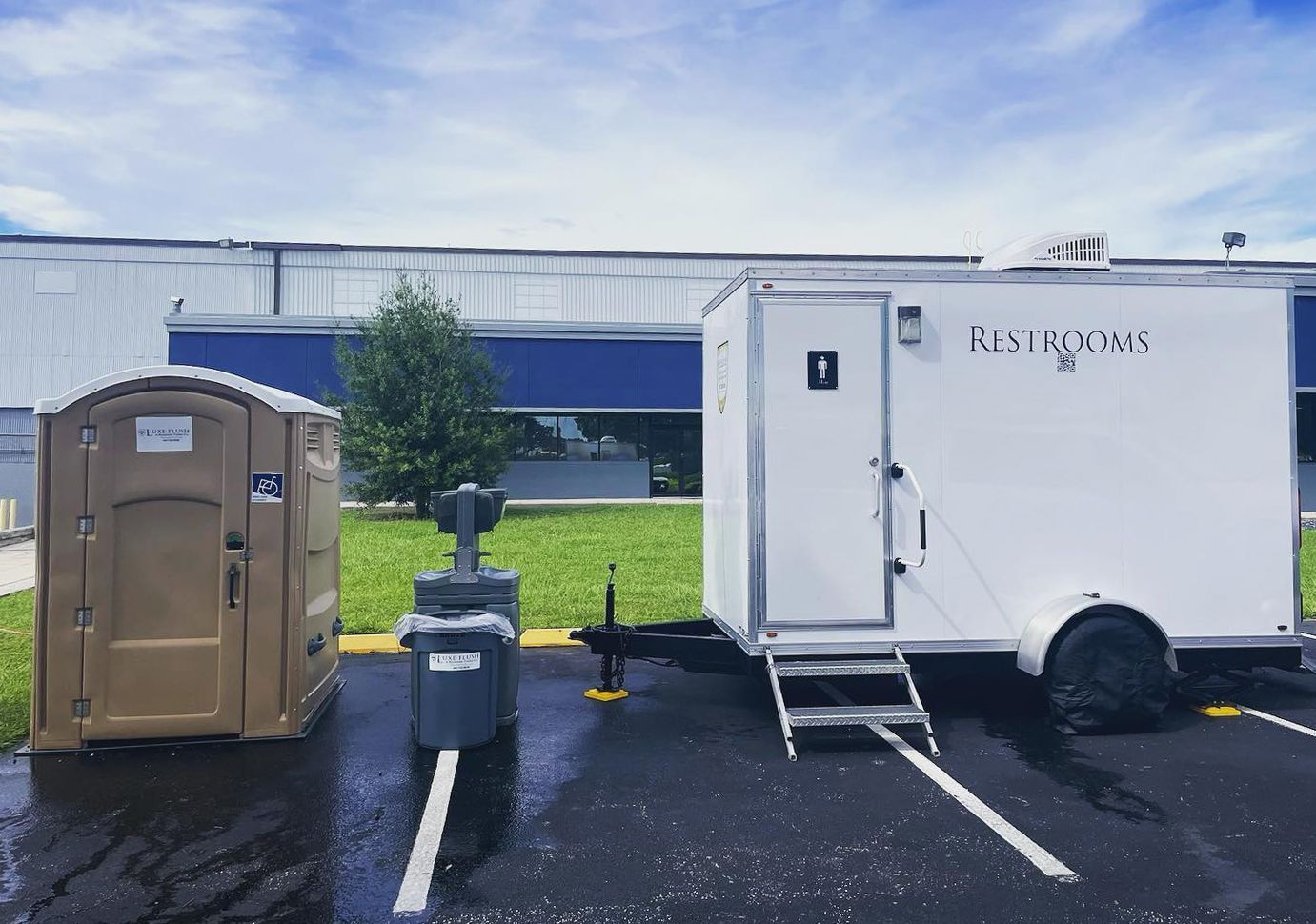Two portable toilets and a trailer are parked in a parking lot