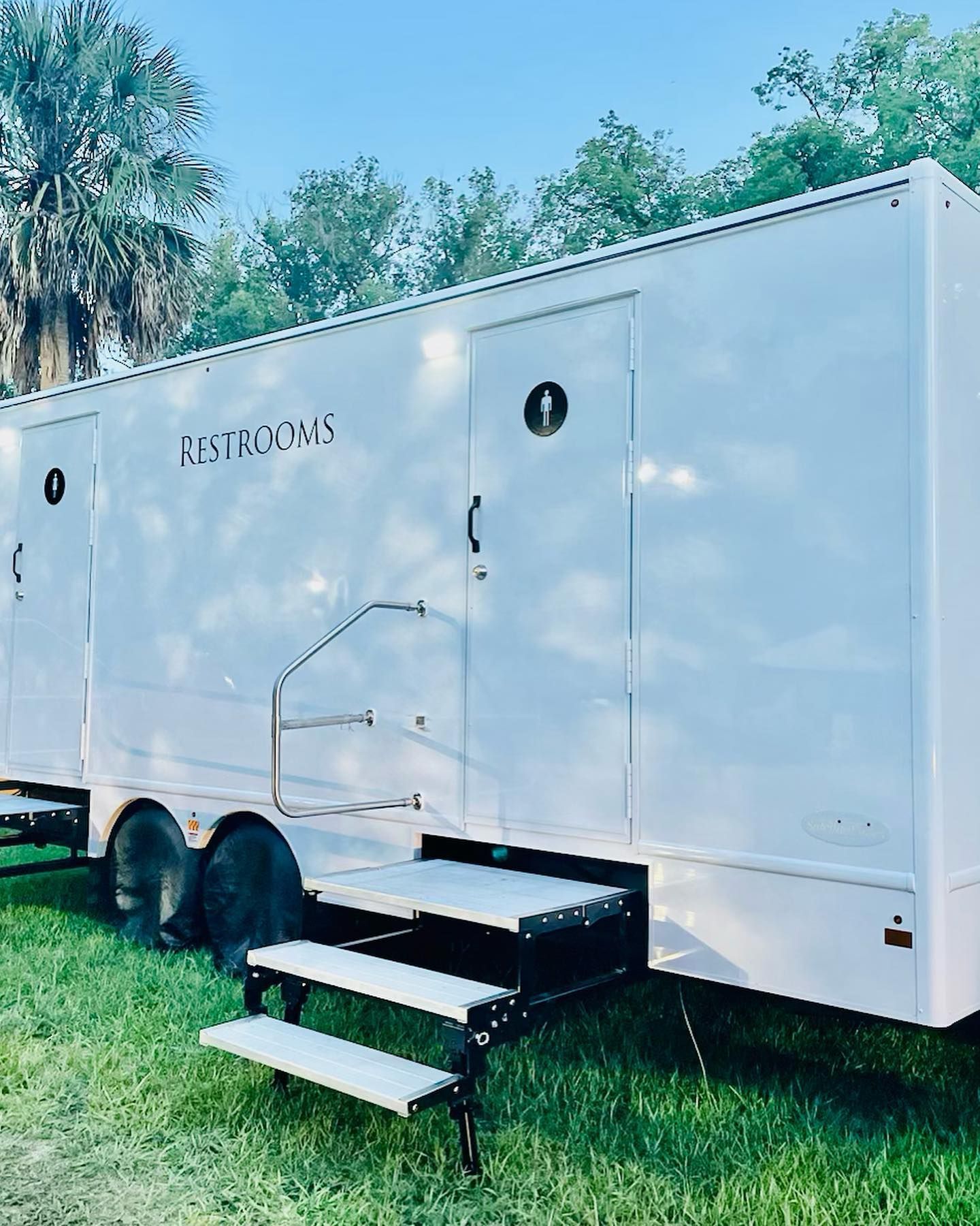 A white trailer with stairs is parked in the grass