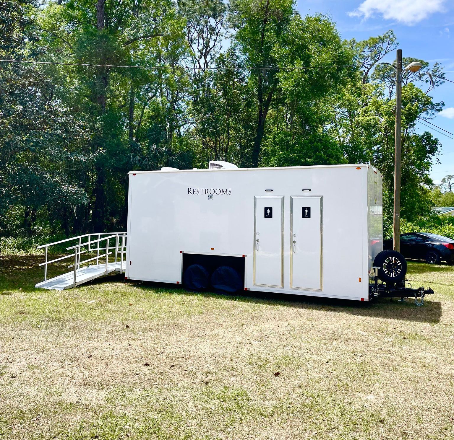 A white trailer with a ramp attached to it is parked in a grassy field