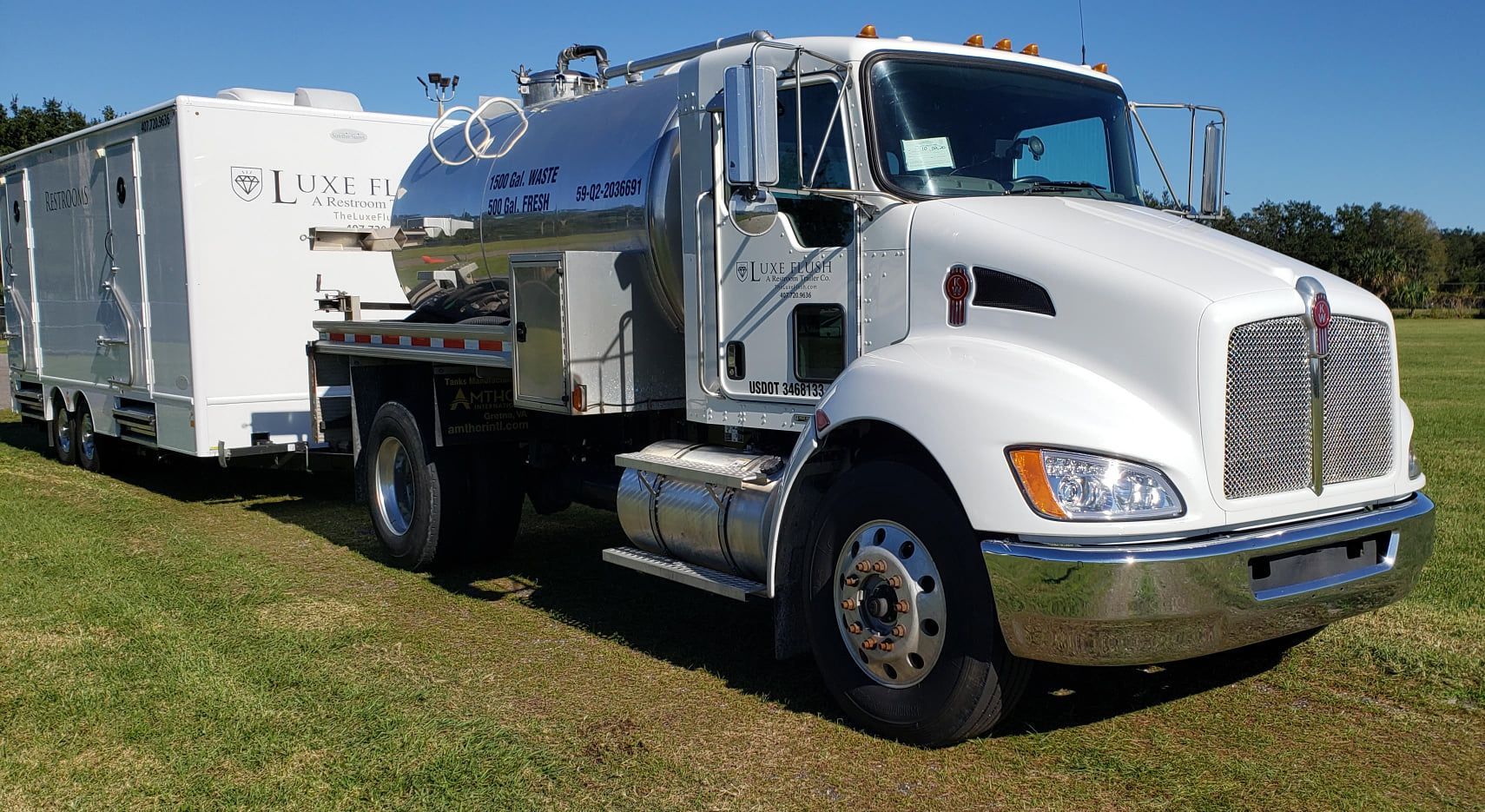 A white truck with a trailer attached to it is parked in a grassy field