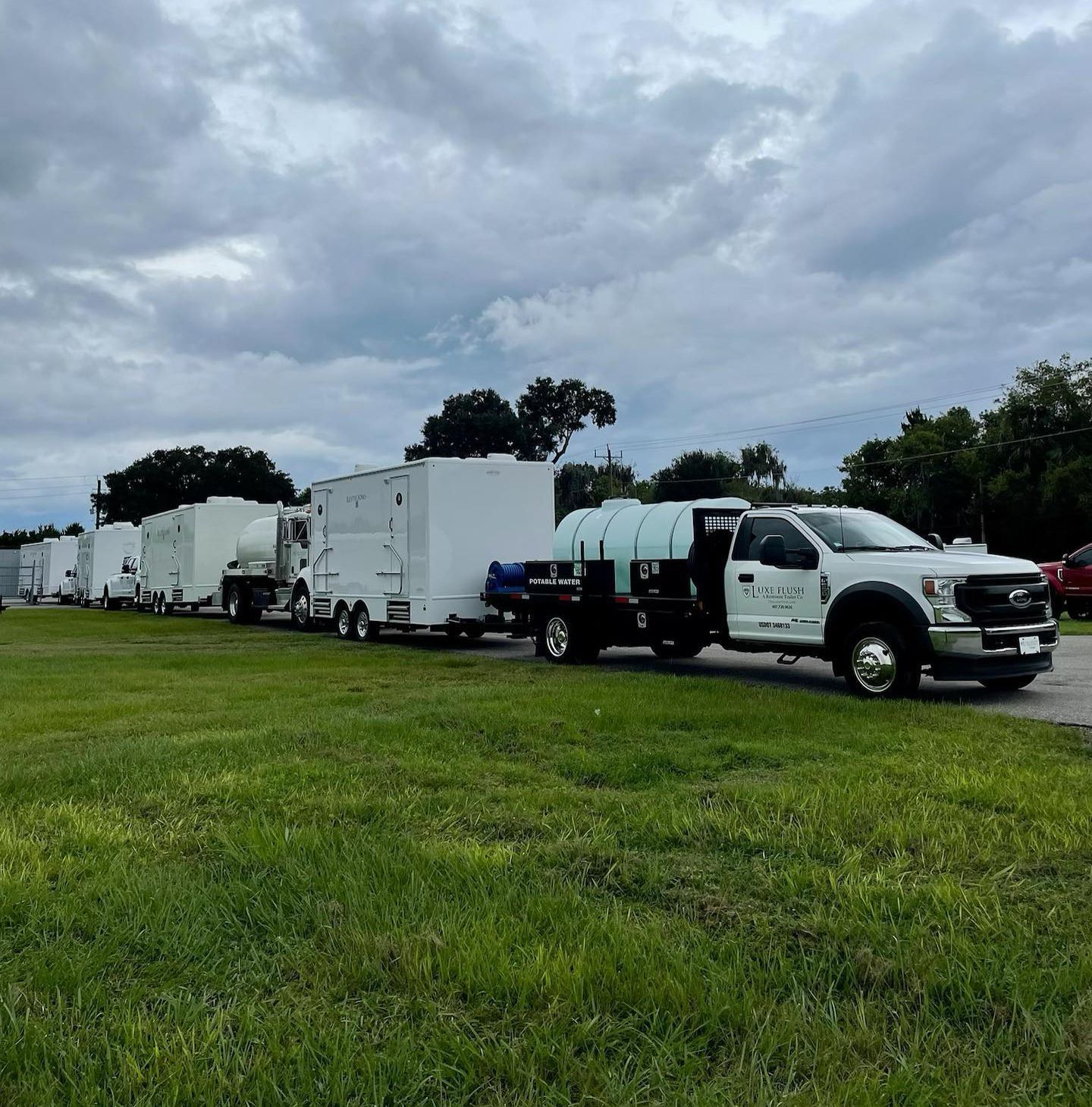 A row of trucks and trailers are parked in a grassy field