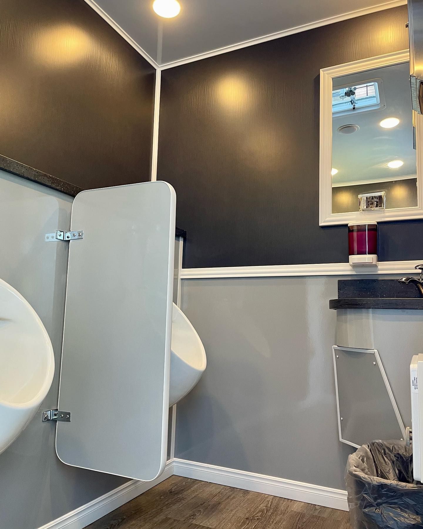 A bathroom with a urinal, sink, mirror, and trash can