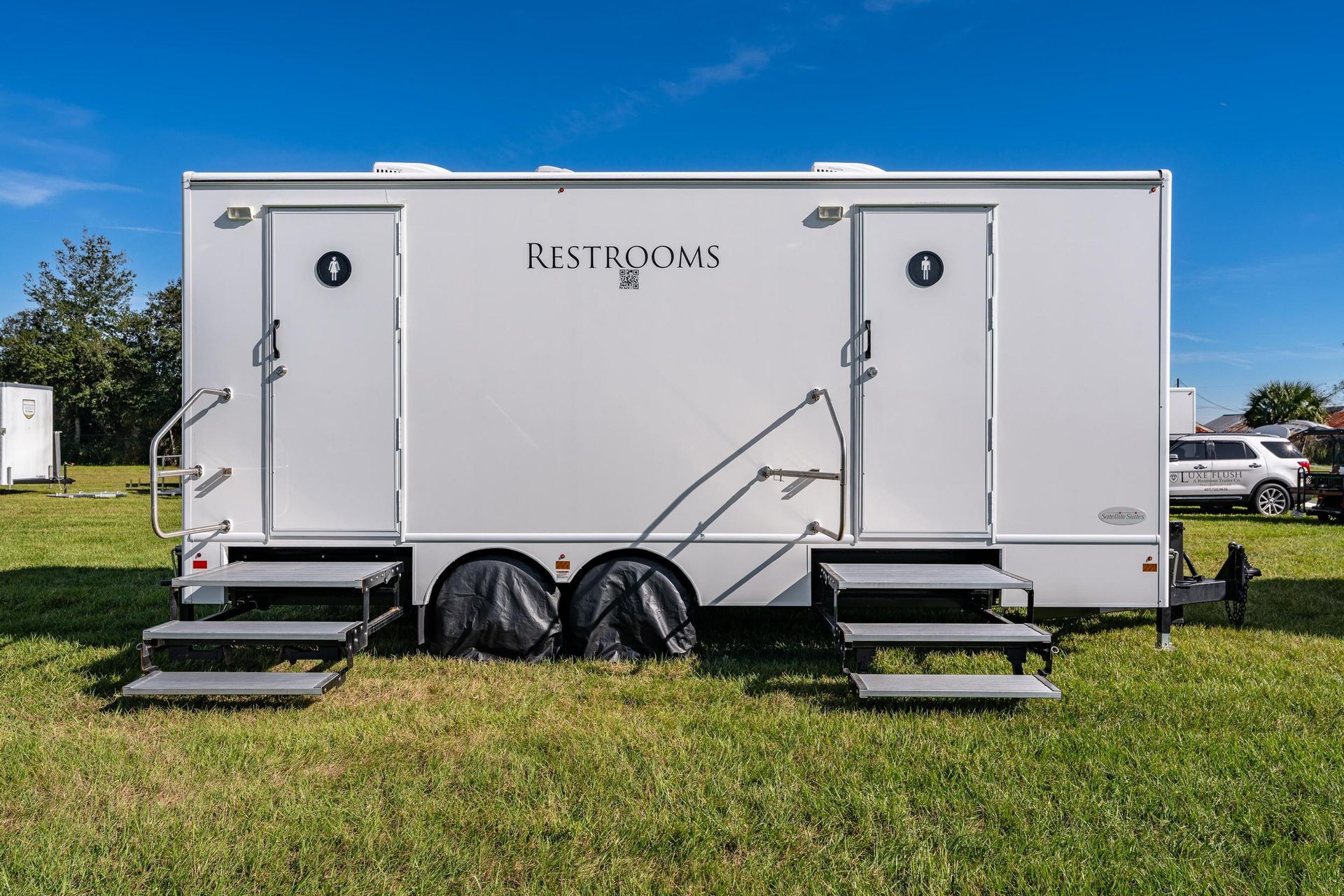 A white restroom trailer is parked in a grassy field