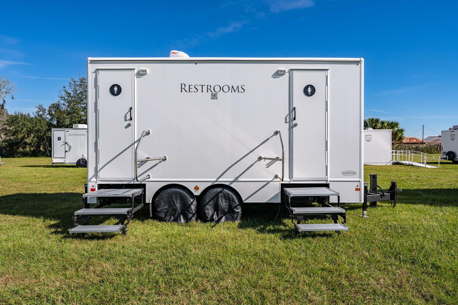 A white trailer with stairs is parked in a grassy field