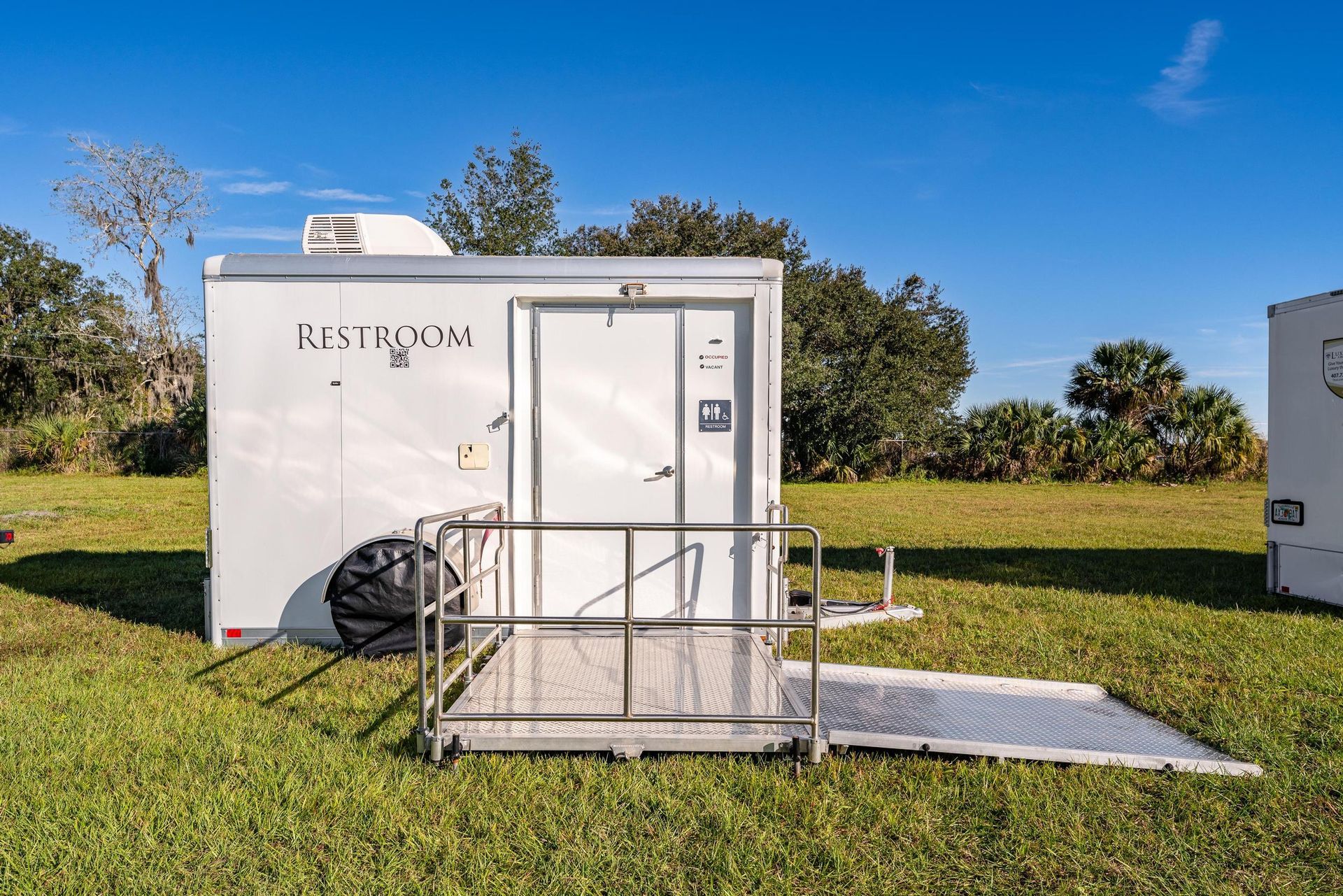 A white trailer with a ramp is sitting in the middle of a grassy field