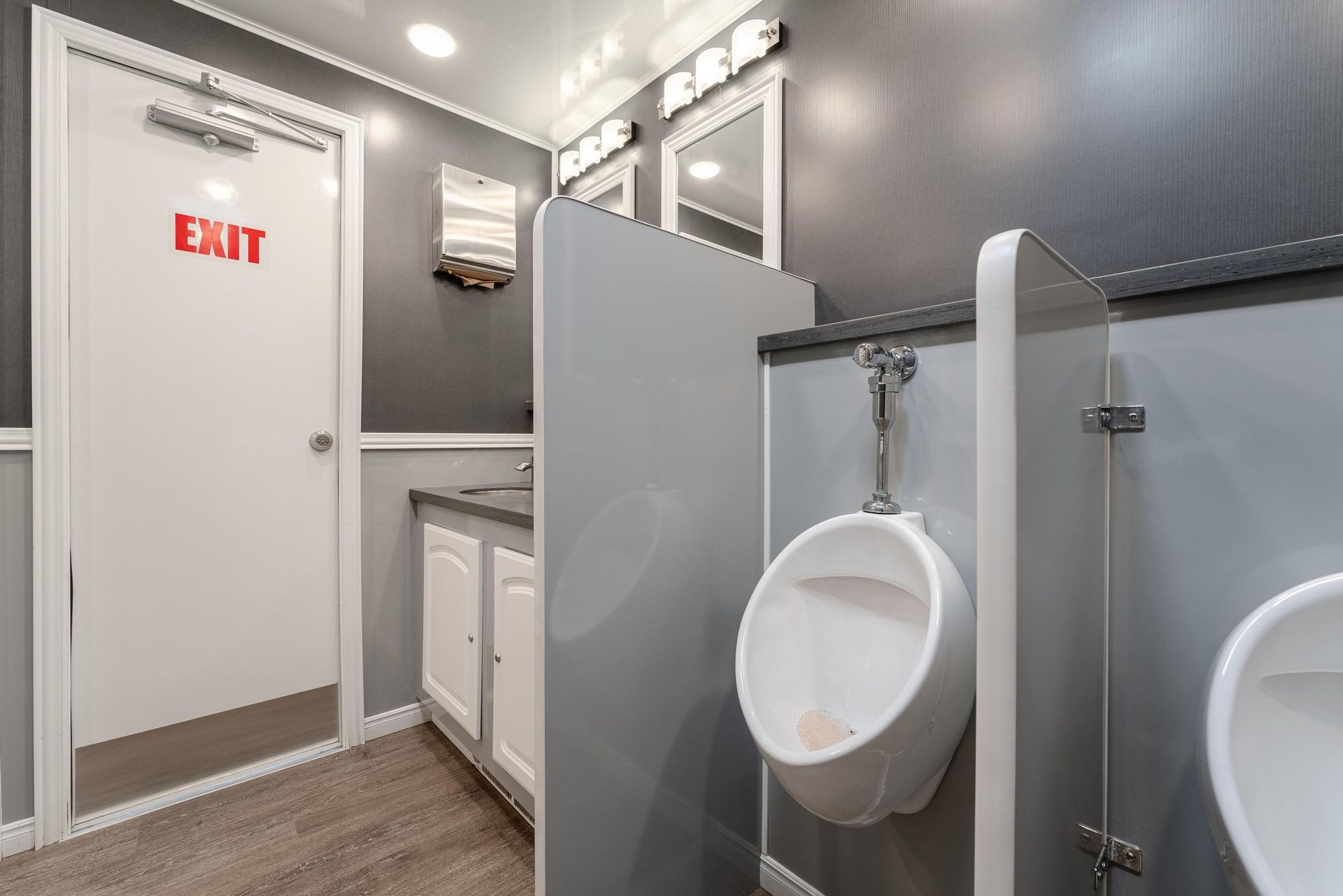 A bathroom with two urinals and an exit sign