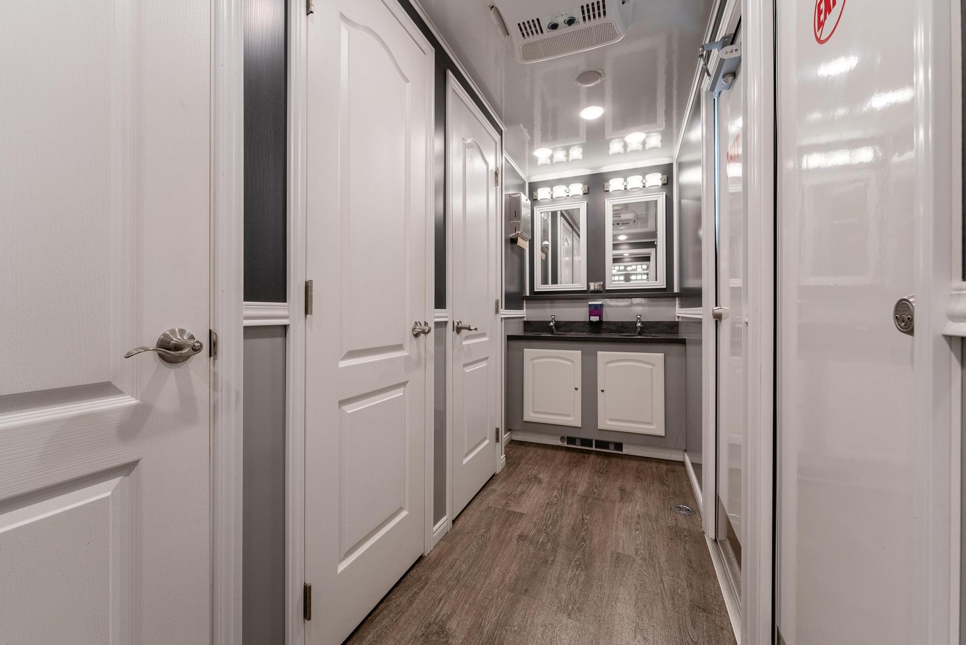 A hallway with white doors leads to a bathroom with a sink and mirrors