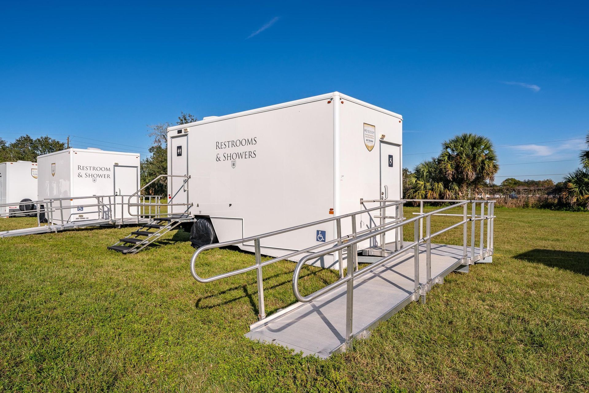 A white trailer with a ramp leading to it is parked in a grassy field