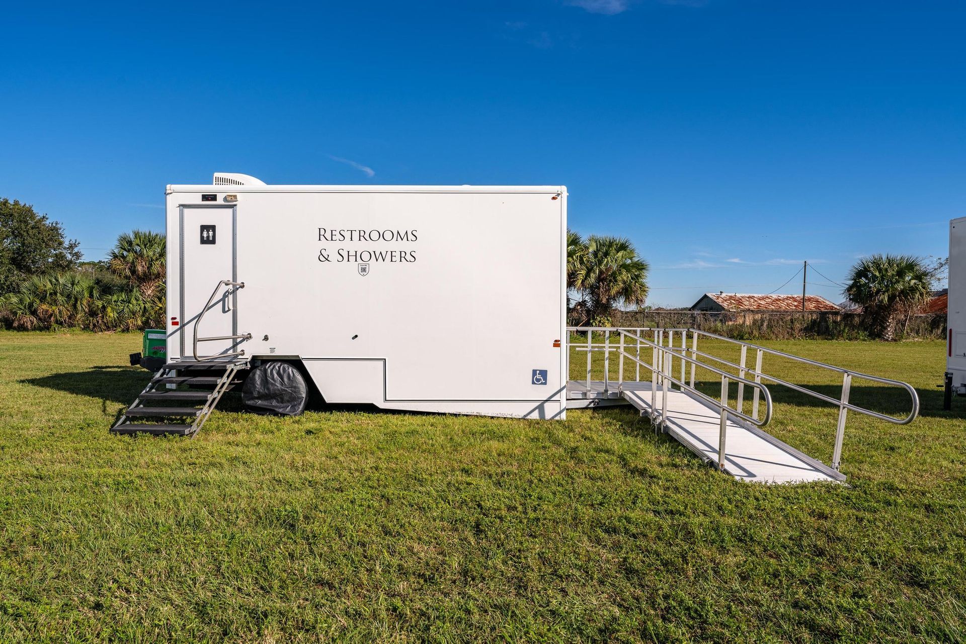 A white trailer with a ramp attached to it is parked in a grassy field