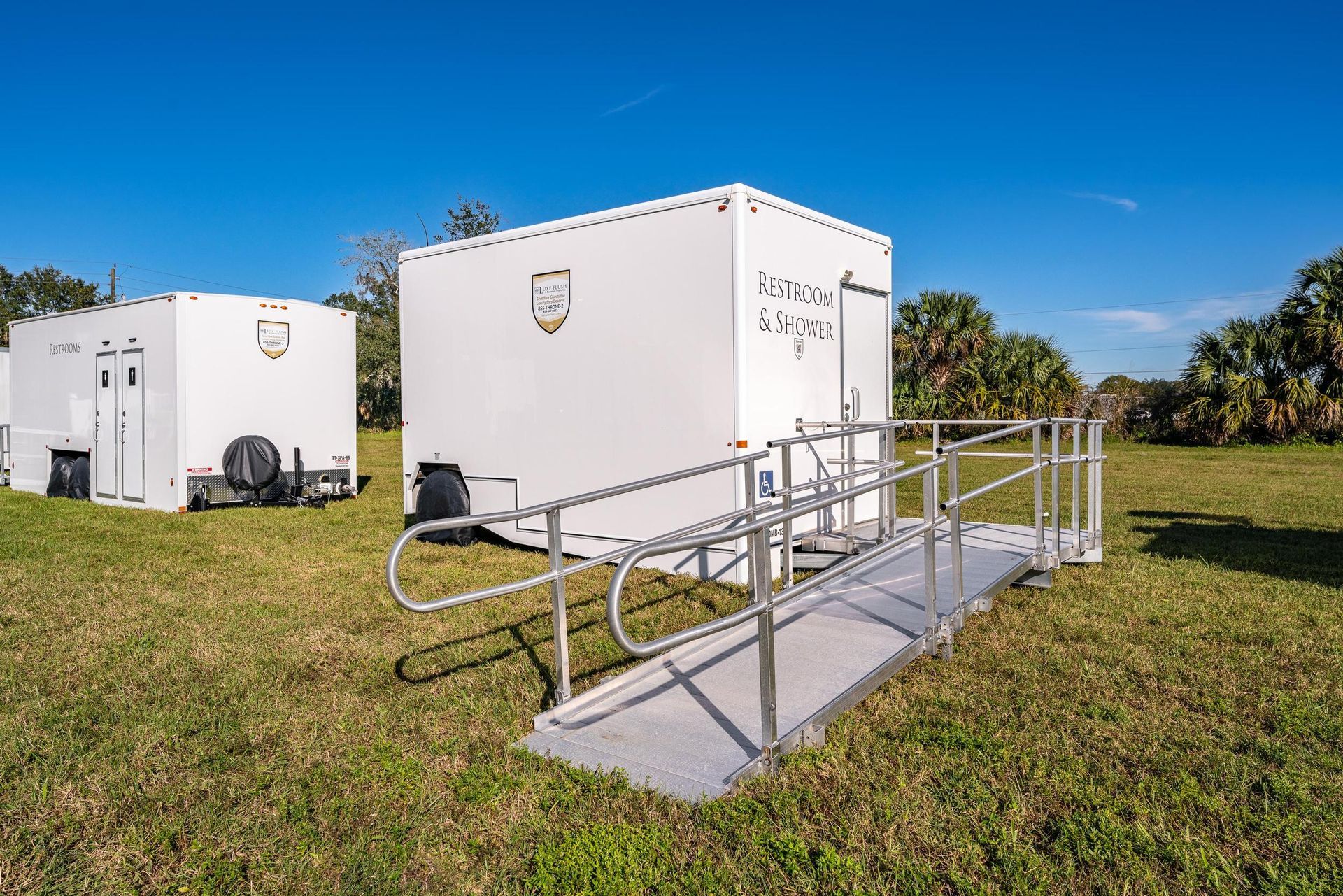 A handicapped ramp is leading to a white trailer in a grassy field