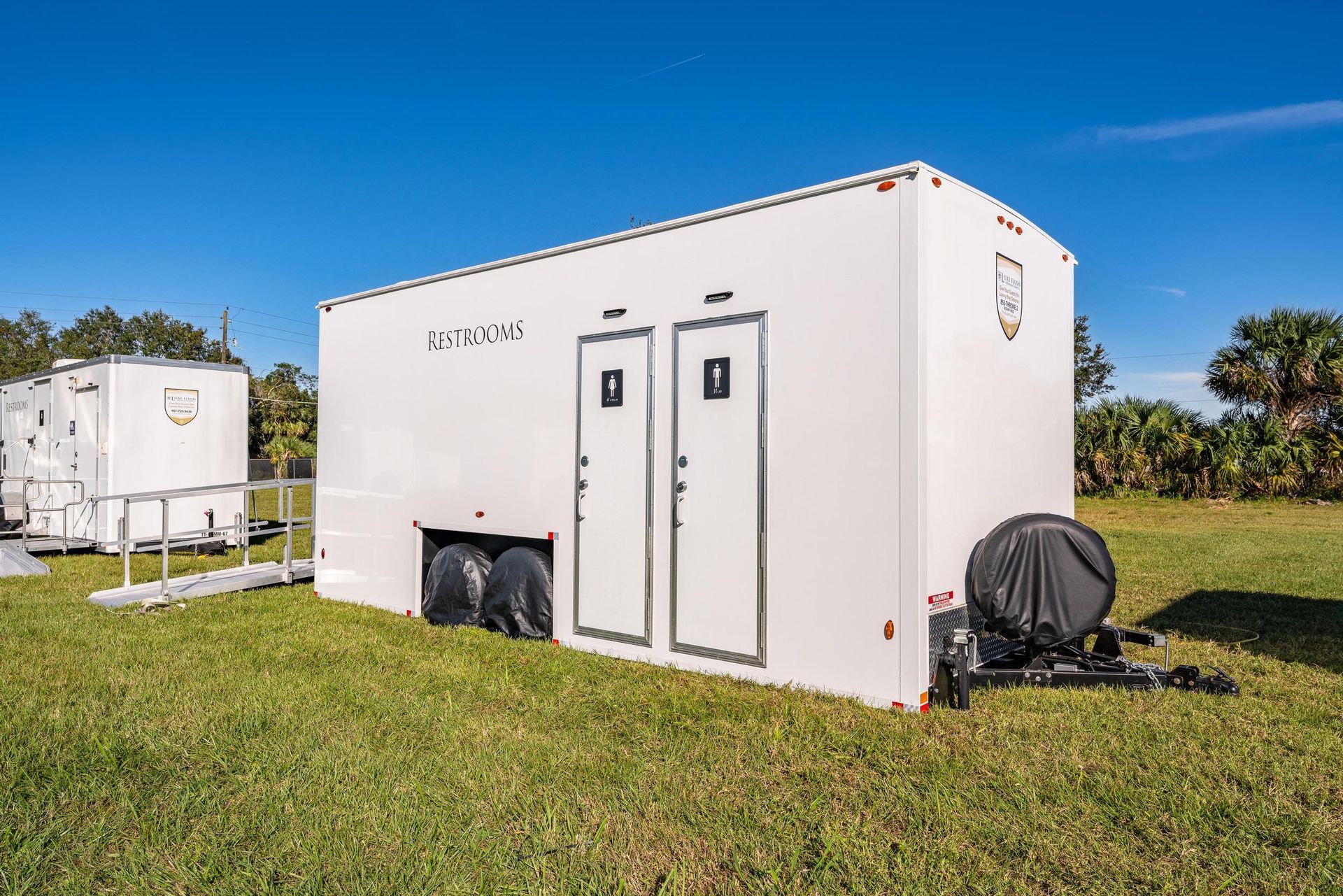 A white trailer with two doors is parked in a grassy field