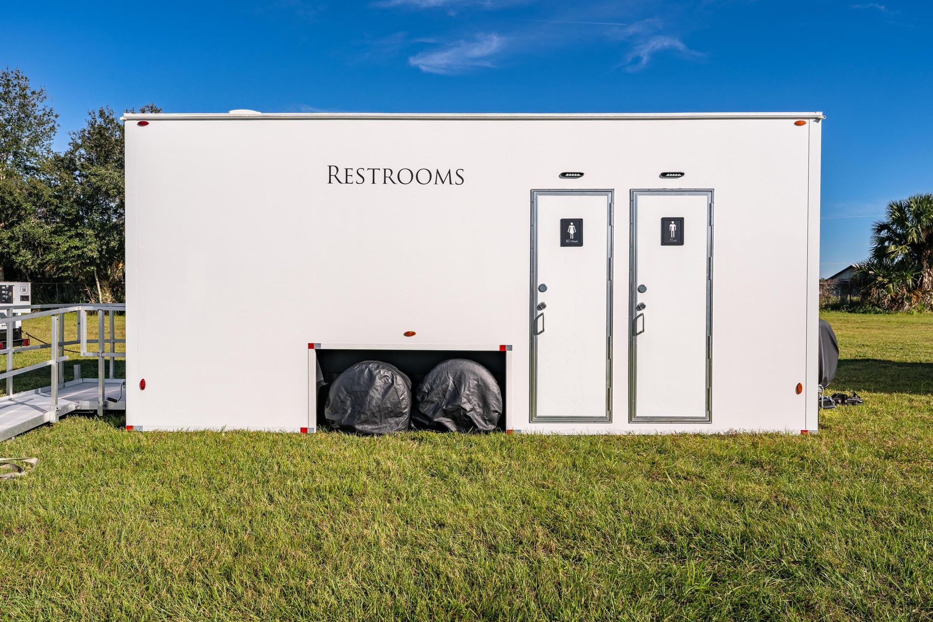 A white trailer with two doors is parked in a grassy field